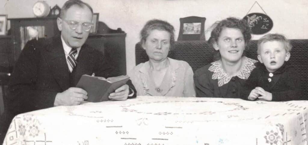 Familie Hempel sitzt mit Enkel Hans im Wohnzimmer und hört Walter Hempel zu, der aus der Bibel vorliest.