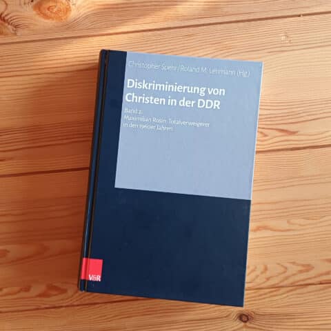 Hardcover-Buch mit dunkelblauem Einband und hellgrauem Titelfeld liegt auf einem hellen Holztisch. Titel: „Diskriminierung von Christen in der DDR, Band 2: Maximilian Rosin: Totalverweigerer in den 1960er Jahren", herausgegeben von Christopher Spehr und Roland M. Lehmann, Verlag V&R.