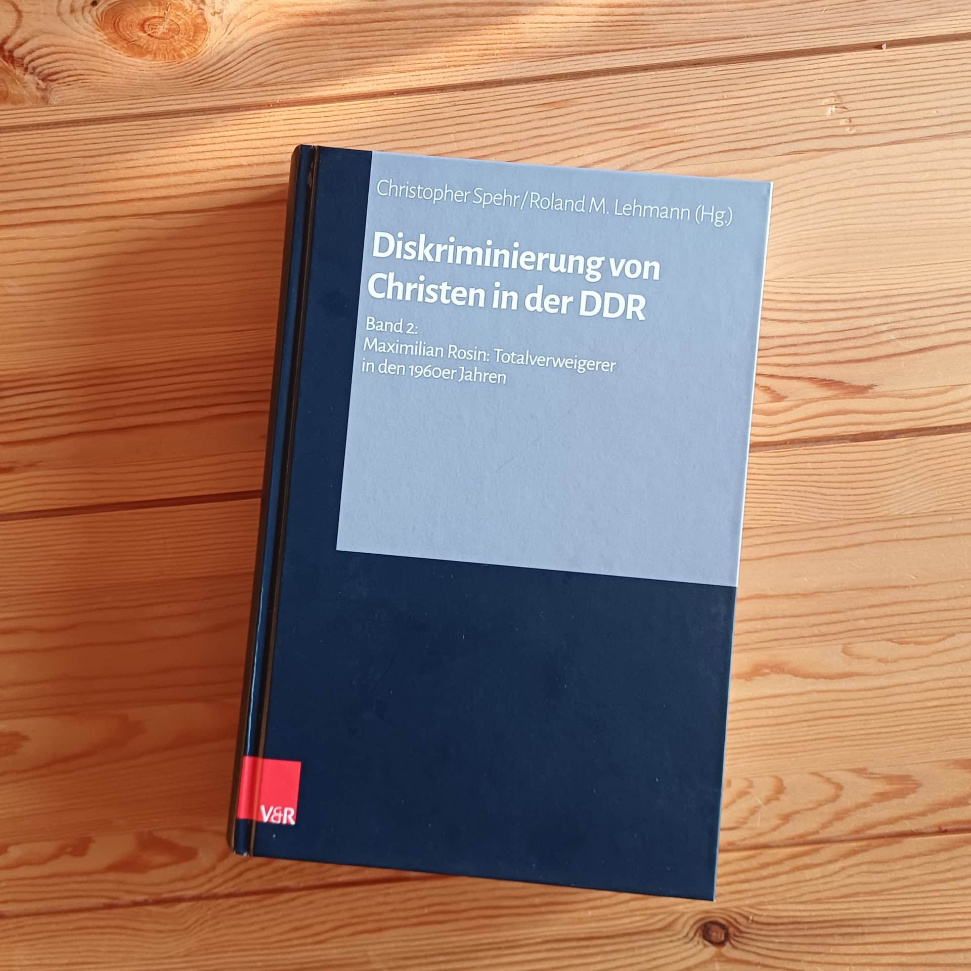 Hardcover-Buch mit dunkelblauem Einband und hellgrauem Titelfeld liegt auf einem hellen Holztisch. Titel: „Diskriminierung von Christen in der DDR, Band 2: Maximilian Rosin: Totalverweigerer in den 1960er Jahren", herausgegeben von Christopher Spehr und Roland M. Lehmann, Verlag V&R.