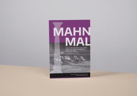 Three-dimensional view of the closed book, standing at a slight angle on a beige surface with a gray background.