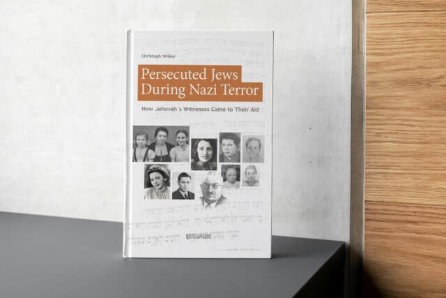 Mockup of the book "Persecuted Jews During Nazi Terror – How Jehovah's Witnesses Came to Their Aid" by Christoph Wilker. The cover features historical black-and-white portrait photographs of Jewish men, women, and children against a background of Hebrew text, with the title on orange panels. Published by Editions Schortgen.
