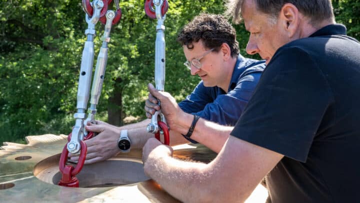 Matthias Leeck und Axel Selbach befestigen mit Spannschlössern und Lasthaken eine bronzene Ronde, die an einem Kran hängt.