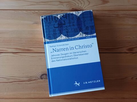 El libro azul «Narren in Christo» de Nathan Schmidtchen sobre una mesa de madera.