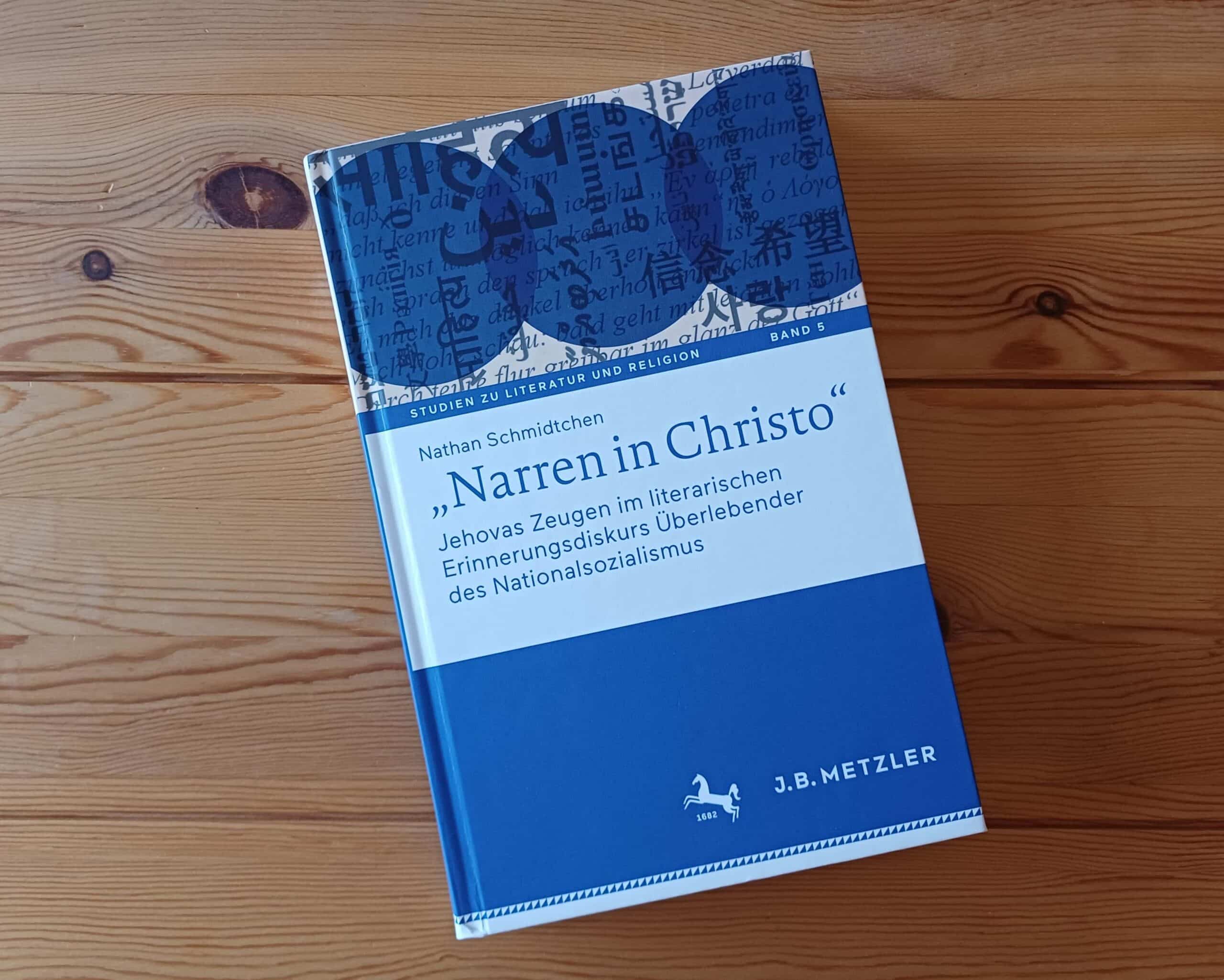 Gros plan du livre « Narren in Christo » de Nathan Schmidtchen sur une table en bois.